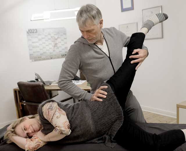 Sieht aus wie Akrobatik: Patient liegt auf der Seite, der Therapeut biegt ein Bein weit nach hinten, eine Technik des thailändischen Chiroflexing