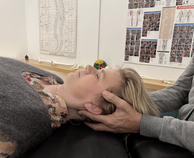 Der Osteopath hält den Kopf der Patientin sanft in Händen, die Patientin liegt entspannt auf dem Rücken